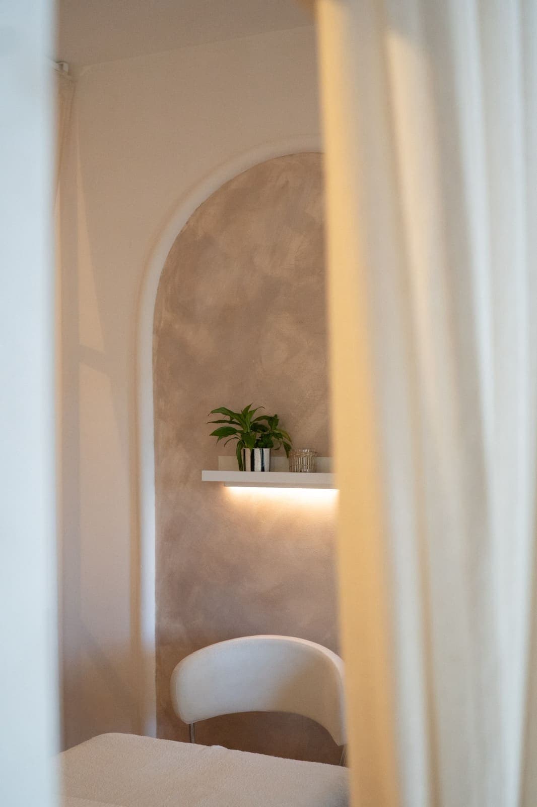 Pogled kroz zavesu na lučnu nišu sa biljkom i toplim svetlom — wellbeing studio Alila u Zemunu